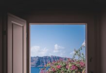 더위를 이기는 집안 관리법 opened window showing outdoor lounger and pink flowers with mountain background