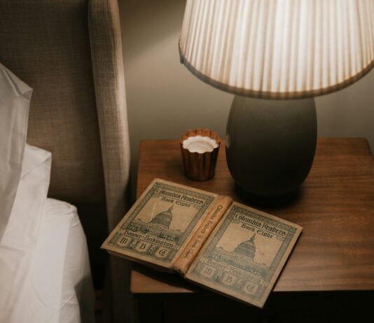 바쁜 일상 속, ‘수면 루틴’이 건강 트렌드로…실생활 적용 팁은? Open book on bedside table with lamp