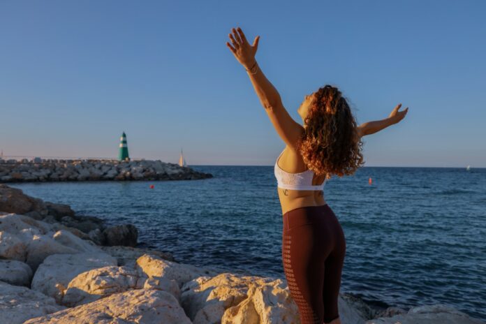 Photo by Mor Shani woman in white sports bra and black bottoms standing on seashore