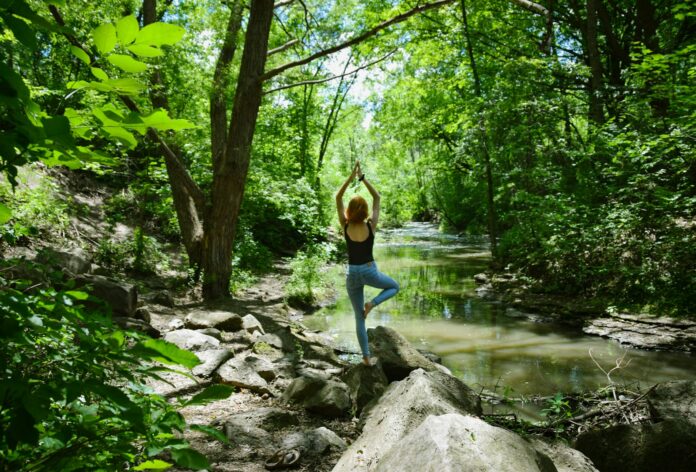 woman in blue tank top and blue leggings standing on gray rock near river during daytime